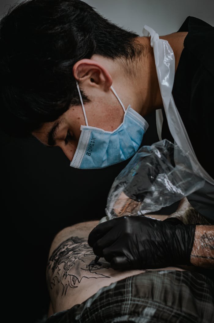 Tattoo artist focusing on intricate design in a Bogotá studio, wearing mask and gloves.