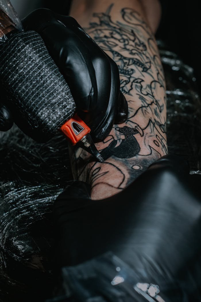 Intricate black tattoo being inked by a gloved artist, showcasing detailed artistry on arm.